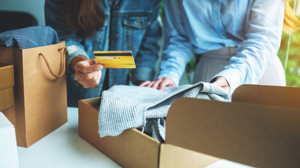 istock wo women holding and using credit card for online shopping while opening a postal parcel box of clothing 1267273191