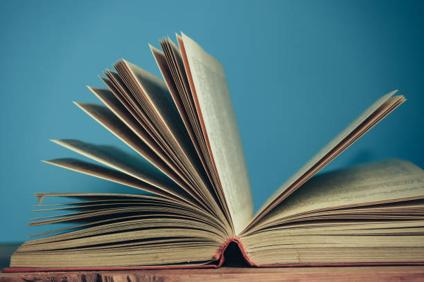 istock Beautiful open book on a red wooden table and blue wall background. 1267273601