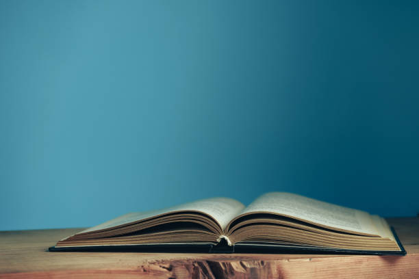 hermoso libro abierto sobre una mesa de madera roja y fondo de pared azul. - bible study university old fashioned fotografías e imágenes de stock