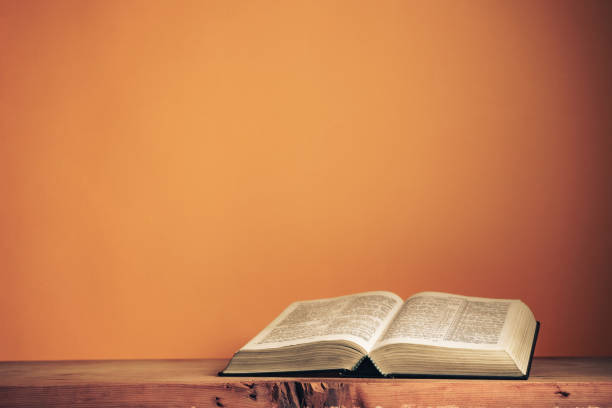 istock Open Holy Bible on a old wooden table. Beautiful orange wall background. 1267274713