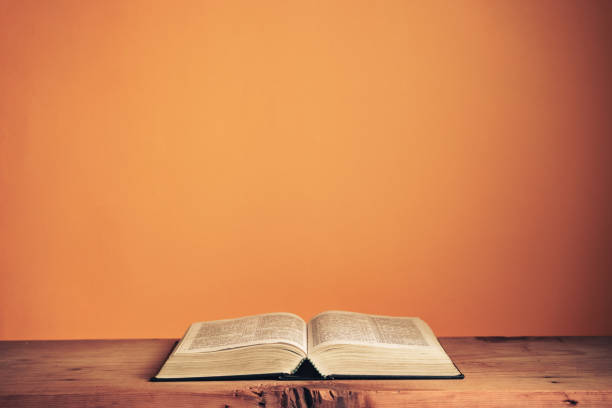 open heilige bijbel op een oude houten lijst. mooie oranje muurachtergrond. - bijbel stockfoto's en -beelden