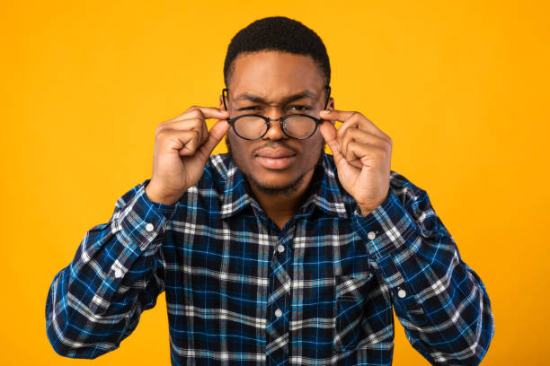 Man In Eyeglasses Looking At Camera Squinting Eyes, Yellow Background Poor Eyesight. Man In Eyeglasses Looking At Camera Squinting Eyes Having Bad Sight Over Yellow Studio Background. squint eyes stock pictures, royalty-free photos & images