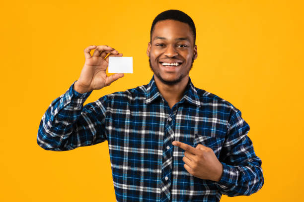 istock Black Guy Holding Blank Visiting Card Standing On Yellow Background 1267275083