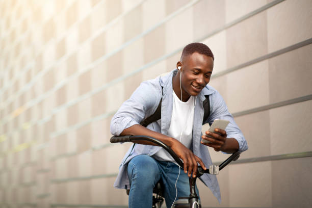 smiling african american guy with bike listening to music from mobile phone near brick wall, free space - extreme sports audio imagens e fotografias de stock