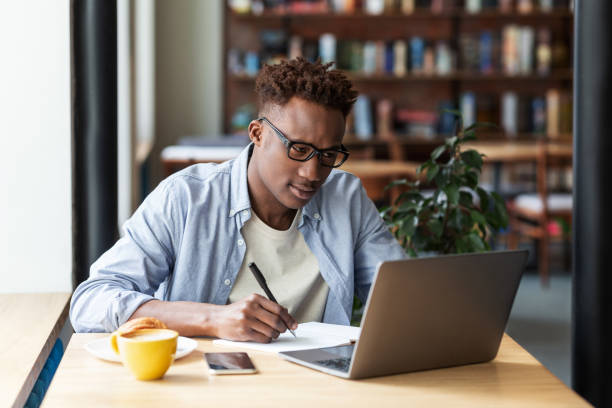 istock Serious black man taking notes while studying online in front of laptop at city cafe 1267275915
