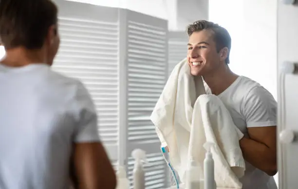 Photo of Confident young man looking in the mirror with towel