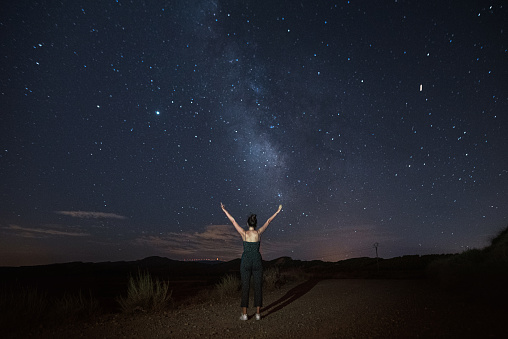 A young woman with arms raised by a starry sky with a visible Milky Way