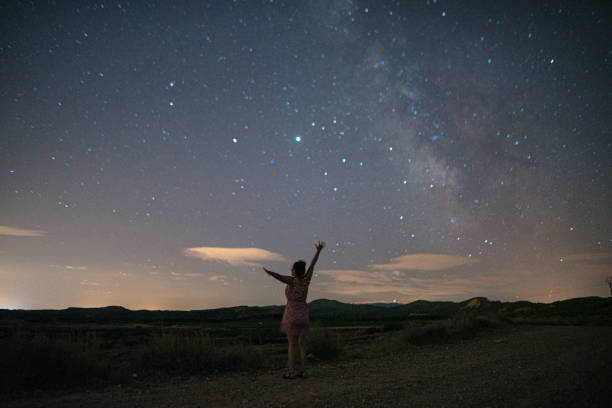 Woman with arms raised by a starry sky with a visible Milky Way A young woman with arms raised by a starry sky with a visible Milky Way scientific exploration stock pictures, royalty-free photos & images