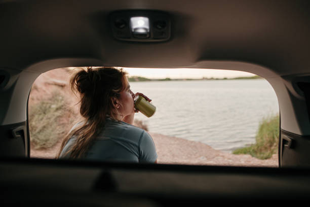 istock Young woman drinking a beverage can while sitting on a car trunk 1267277540