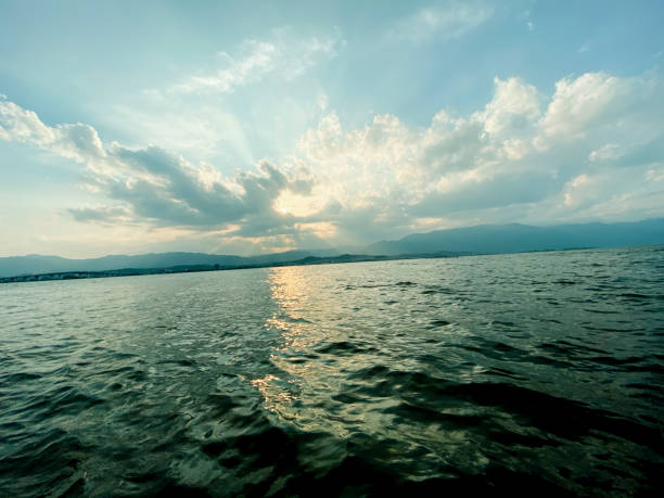 Evening view of the sun, clouds and waves on the lake that sinks in the mountains.