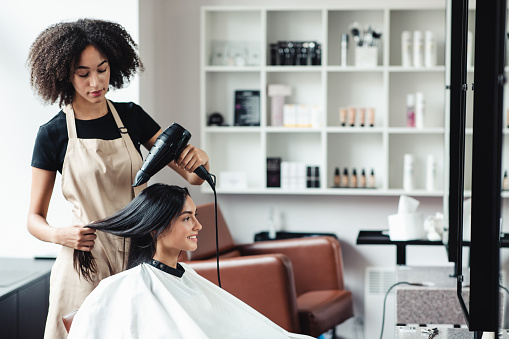 At beauty salon. African american hairdresser drying hair of young customer, empty space