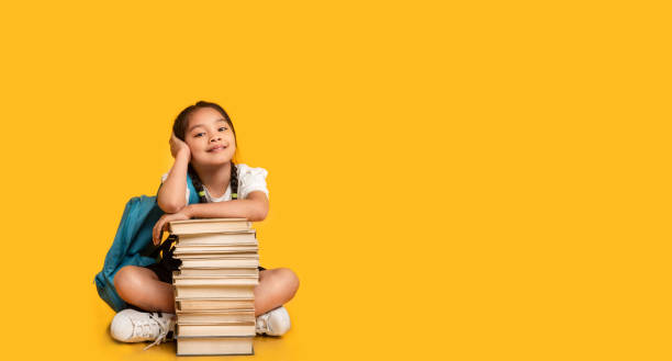 istock Asian Elementary Student Girl Sitting At Books Stack, Yellow Background 1267279292