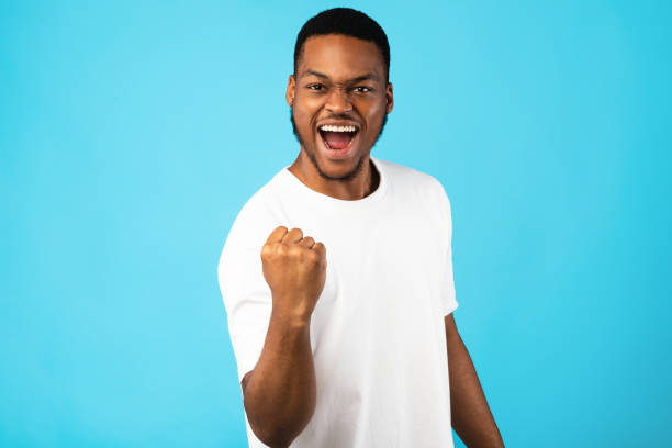 African Man Shaking Fist Gesturing Yes Celebrating Success, Studio Shot Joy Of Victory. African Man Shaking Fist Gesturing Yes Celebrating Success Over Blue Background. Studio Shot black man stock pictures, royalty-free photos & images