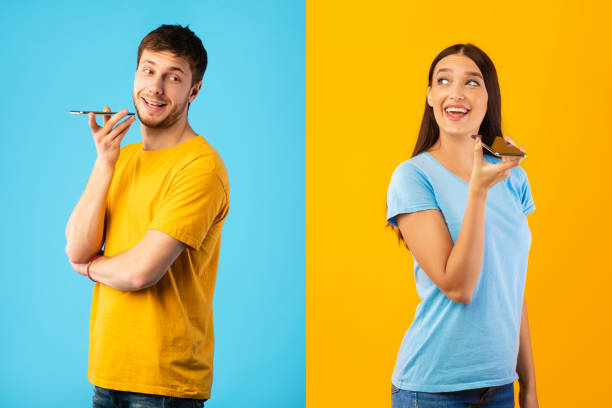 Portrait of couple talking on phone using speaker Communication Concept. Couple talking on phone holding gadget near mouth, posing on studio wall two men same clothes stock pictures, royalty-free photos & images
