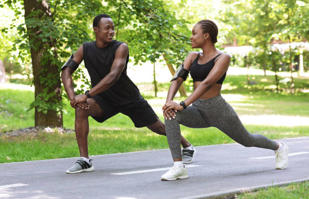 casal negro esportivo se preparando para maratona juntos, alongando músculos antes de correr ao ar livre - couple stretching running jogging - fotografias e filmes do acervo
