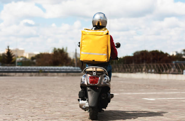 courier con mochila amarilla montar scooter de vuelta a la cámara al aire libre - ciclomotor vehículo de motor fotos fotografías e imágenes de stock