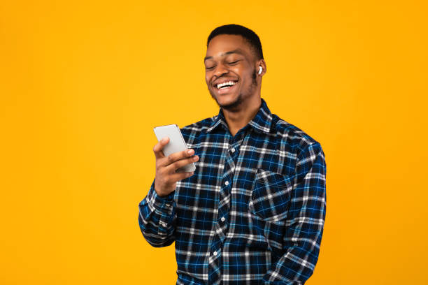 istock Black Man Laughing Listening To Audiobook Using Smartphone, Yellow Background 1267284169
