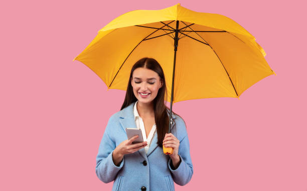 携帯電話を使って傘を持つ笑顔の若い女の子の肖像画 - rain women umbrella parasol ストックフォトと画像