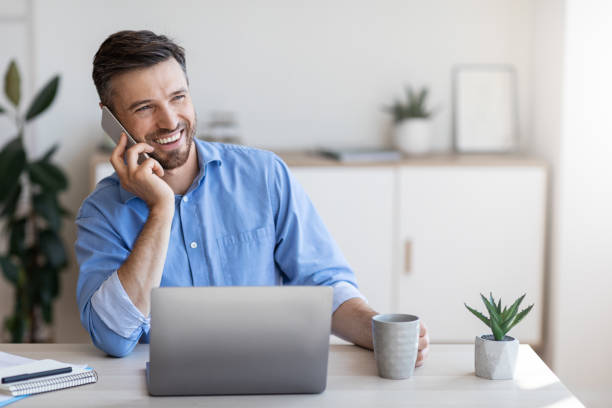 istock Smiling Male Office Employee Talking On Cellphone And Drinking Coffee At Workplace 1267286674