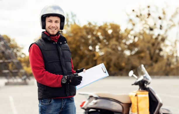 istock Courier Man Holding Folder And Pen Standing Near Scooter Outside 1267287140