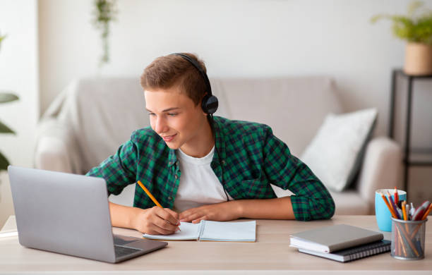 istock Joyful teen guy writing at notebook and looking at laptop 1267287179