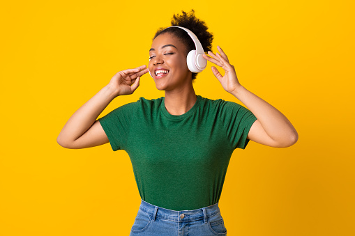 Enjoy The Sound. Portrait of black woman listening to music in headphones with closed eyes, touching headset