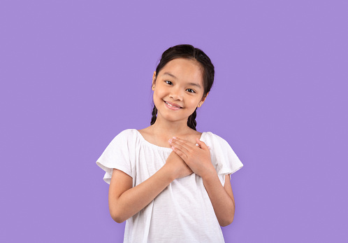 Gratitude. Thankful Chinese Girl Pressing Hands To Chest Smiling To Camera Posing Over Purple Background. Studio Shot