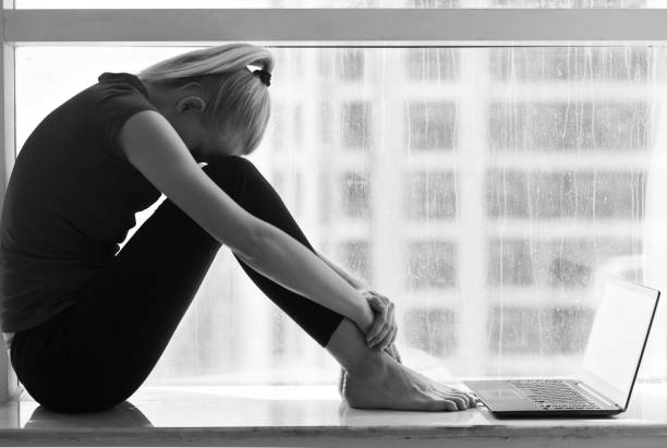 mulher triste sentada com um laptop perto da janela da cidade. depressão e desespero. - failure relationship difficulties computer women - fotografias e filmes do acervo