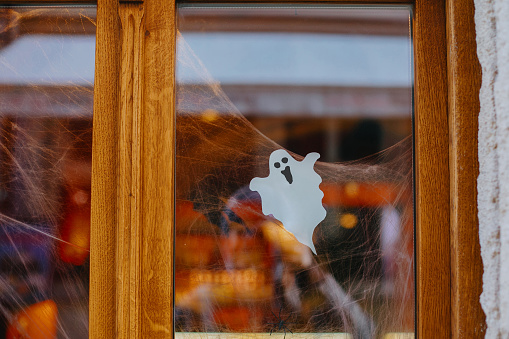 Halloween street decor. Paper cut ghost and cobweb on door or window at store, festive decoration of city street. Happy Halloween