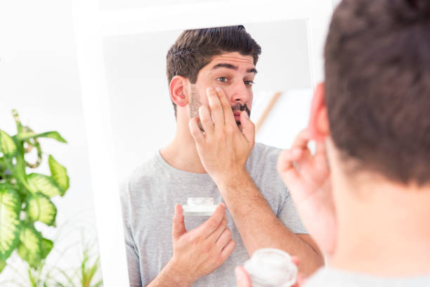 istock Man applying cream onto his face while standing in the bathroom 1267300119