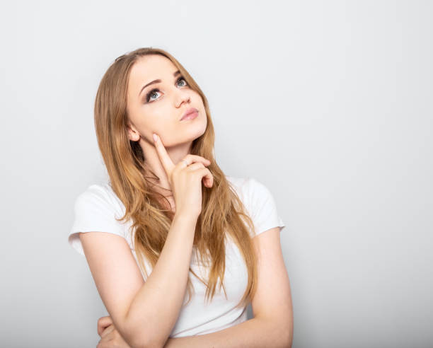 istock Thinking blond doubt young woman looking up and thinking on light blue background. Closeup portrait 1267300169
