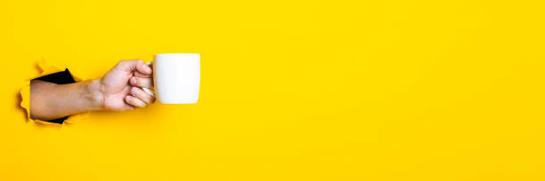 istock Man's hand holding a white cup on a bright yellow background. Banner. 1267302753