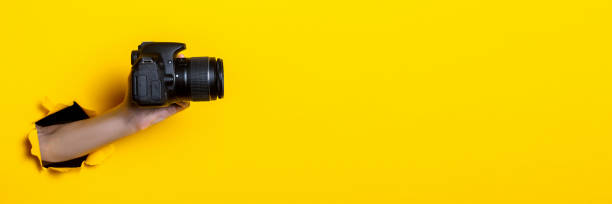 istock Female hand holding a camera on a bright yellow background. Banner. 1267303714