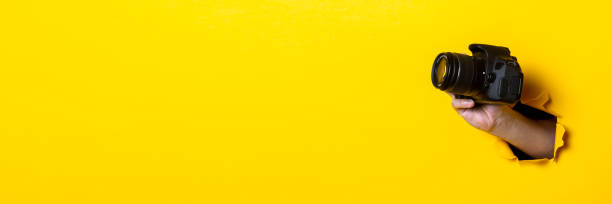 istock Man's hand holding a camera on a bright yellow background. Banner. 1267303820