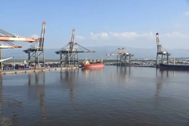 View on Kingston Harbour in Jamaica is the seventh-largest natural harbour in the world. In the background are gantry cranes and red general bulk cargo vessel and blue container ship.
