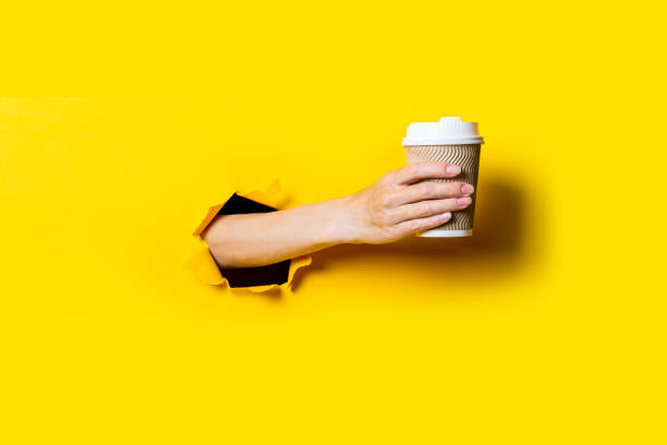 istock Woman's hand holds paper cup with coffee on bright yellow background. 1267305203