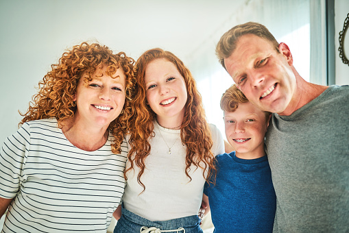 Cropped portrait of an affectionate family of four smiling while standing in their living room at home