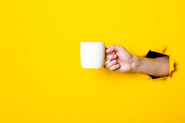 istock Man's hand holding a white cup on a bright yellow background 1267306026