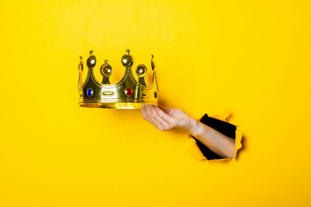 istock Female hand holds a gold crown on a bright yellow background. 1267306239