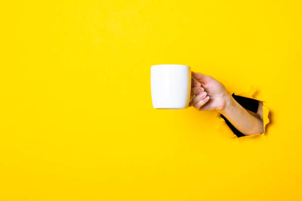 istock Woman's hand holding a white cup on a bright yellow background 1267306342