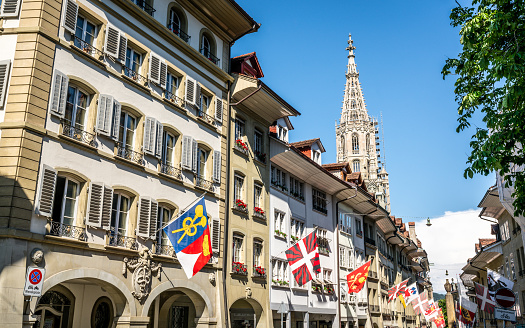 Scenic view of old buildings with city flags and Bern Minster cathedral tower in Bern old town Switzerland