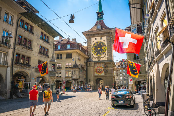 widok na starą ulicę z flagami turystów i wieżą zegarową zytglogge na ulicy kramgasse w bernie staromiejskiej szwajcarii - berne canton zdjęcia i obrazy z banku zdjęć