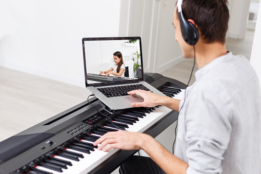 A man learning to play piano online with a computer staying at home. Concepts of self taught, staying at home and working online