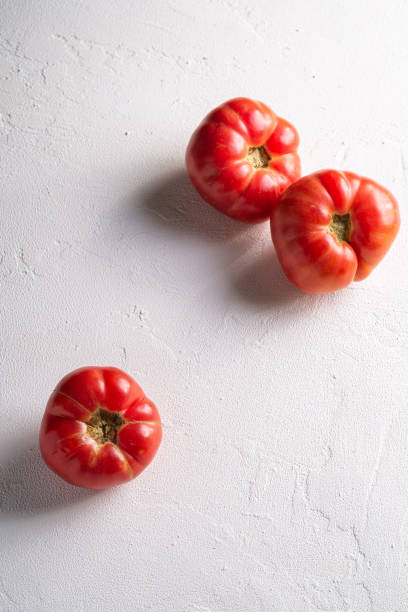 drei rosa erbstück tomatengemüse, frische rote reife tomaten, vegane lebensmittel, weißer stein beton hintergrund, winkelansicht selektiven fokus - tomato beefsteak tomato heirloom tomato pink stock-fotos und bilder
