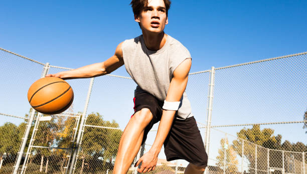 Teen athlete playing basketball at the outdoor court. College sports player. Young male teenager playing street basketball focused exercising dribbling the ball at the outdoor court on a sunny summer day. college basketball court stock pictures, royalty-free photos & images