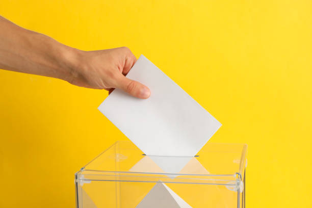 istock Man putting ballot into voting box on yellow background 1267314117