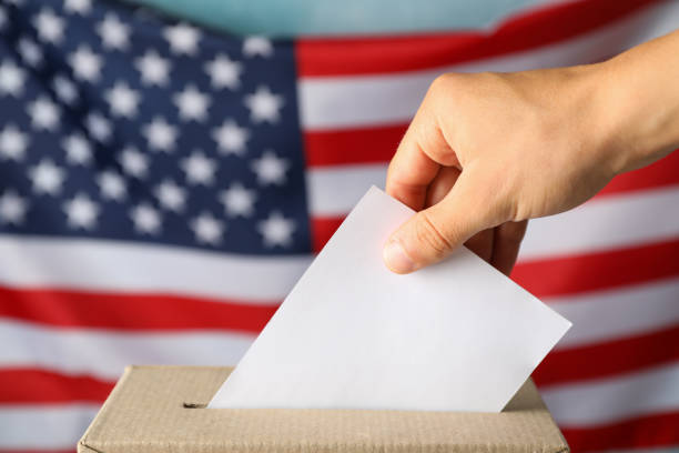 istock Man putting ballot into voting box against american flag 1267315481