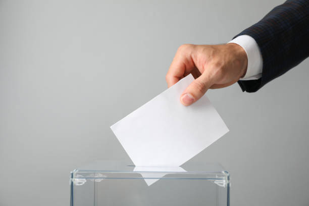 istock Man putting ballot into voting box on gray background 1267315816