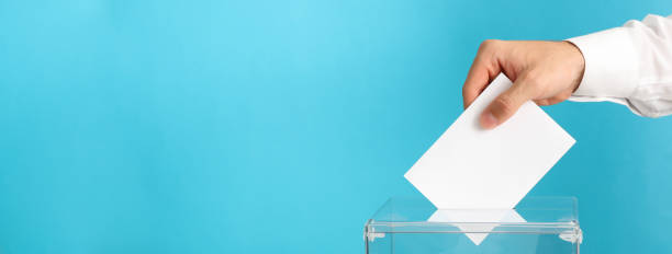 istock Man putting ballot into voting box on blue background 1267316040