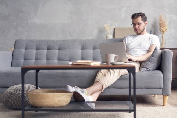 istock Typing new blog post. Handsome young man using his laptop with smile while sitting on the couch at home. 1267317317